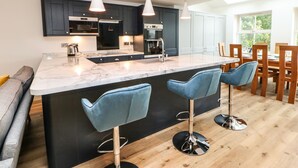 A modern kitchen with a marble island, pendant lights, and bar stools. - Bramblewood Cottage (Barnard Castle)