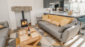 A modern living room with a grey sofa, a wooden coffee table, and a stone fireplace. - Bramblewood Cottage (Barnard Castle)