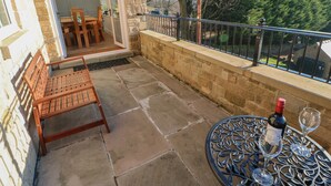 A balcony with a stone wall, a wooden chair, a metal table, and a bottle of wine. - Bramblewood Cottage (Barnard Castle)