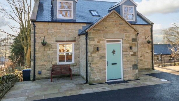 A stone house with a pitched roof, a front door, and a bench outside. - Bramblewood Cottage (Barnard Castle)
