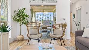 Una sala de estar moderna con una mesa redonda, dos sillas de mimbre, un sofá y una planta grande en maceta.