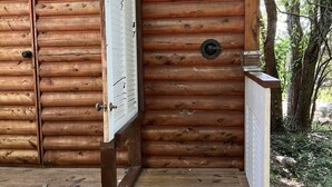 Una cabaña de madera con puerta de madera, un porche pequeño y un perro acostado en el porche.