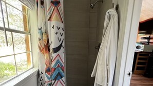 Un área de ducha con cortina de baño estampada, una toalla blanca colgada en la pared y una ventana con persianas.