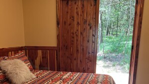 Un dormitorio con una cama grande, una puerta de madera que da a un balcón y vistas a zonas verdes.