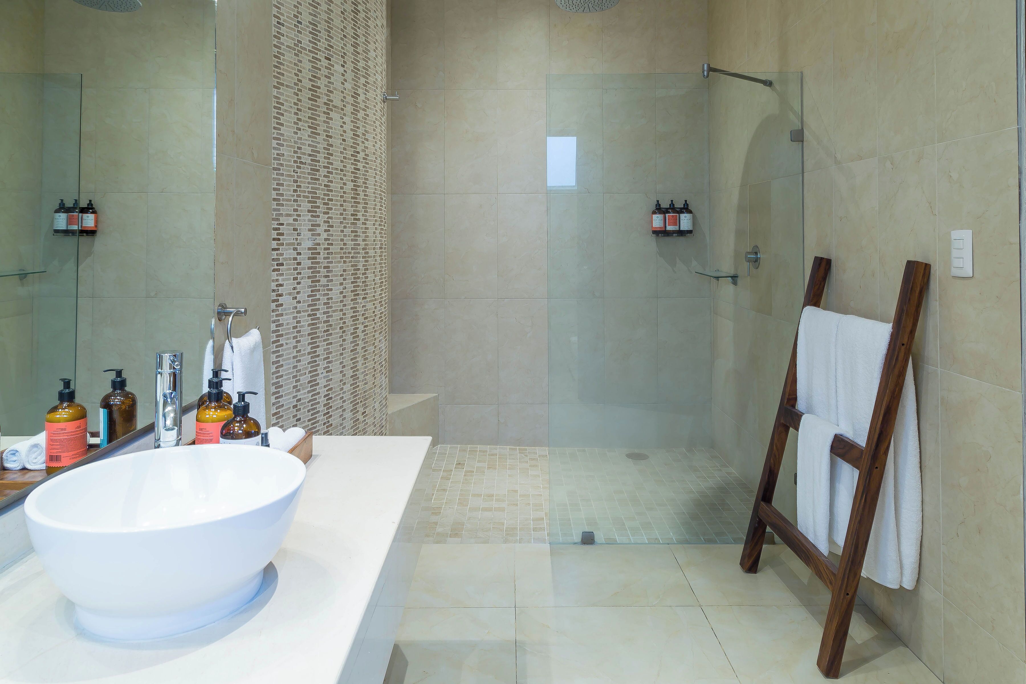 A modern bathroom with a large white sink, glass shower enclosure, and a wooden towel rack.