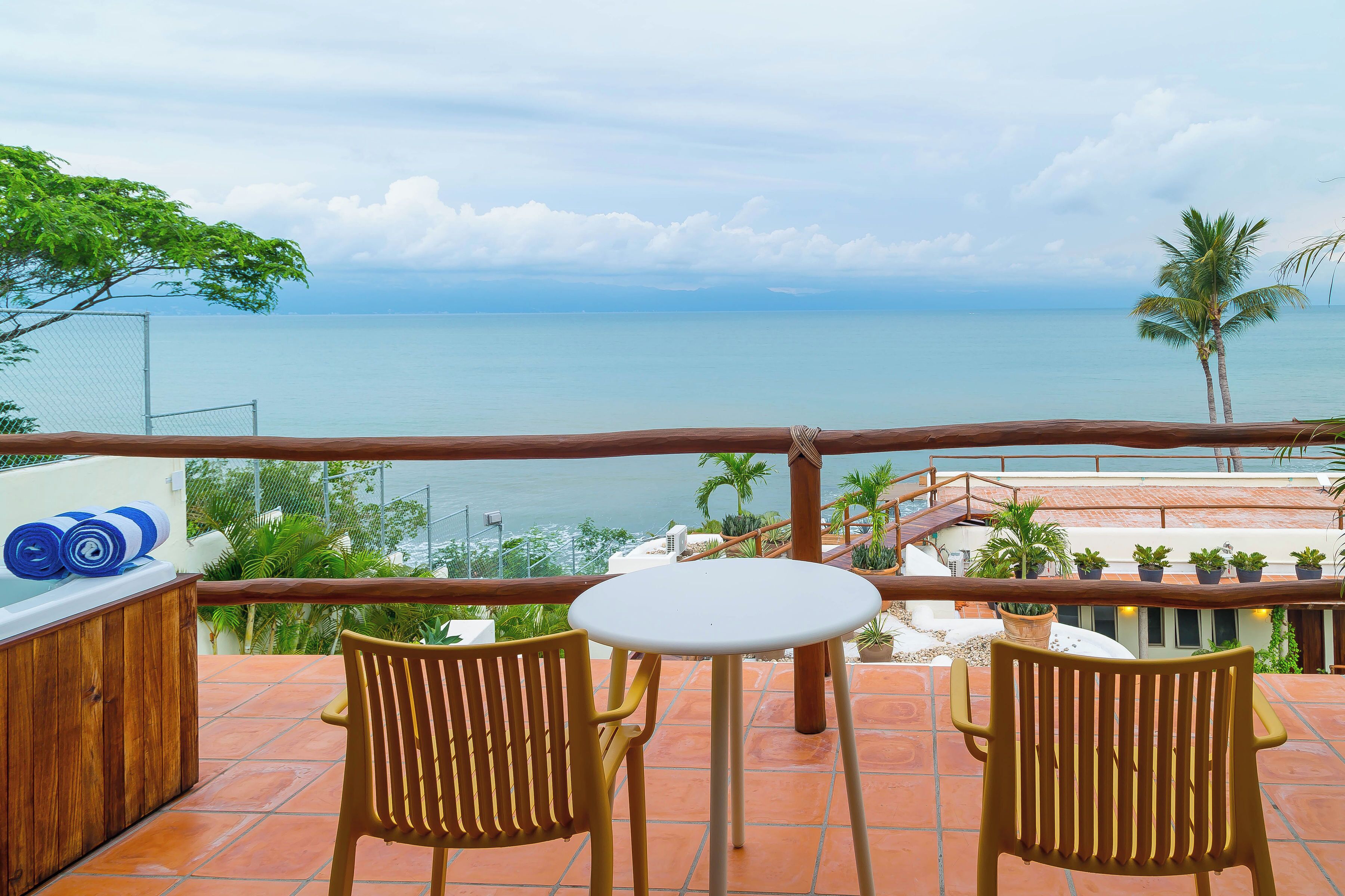 Una terraza con una mesa y dos sillas, con vista a un cuerpo de agua y al paisaje costero.