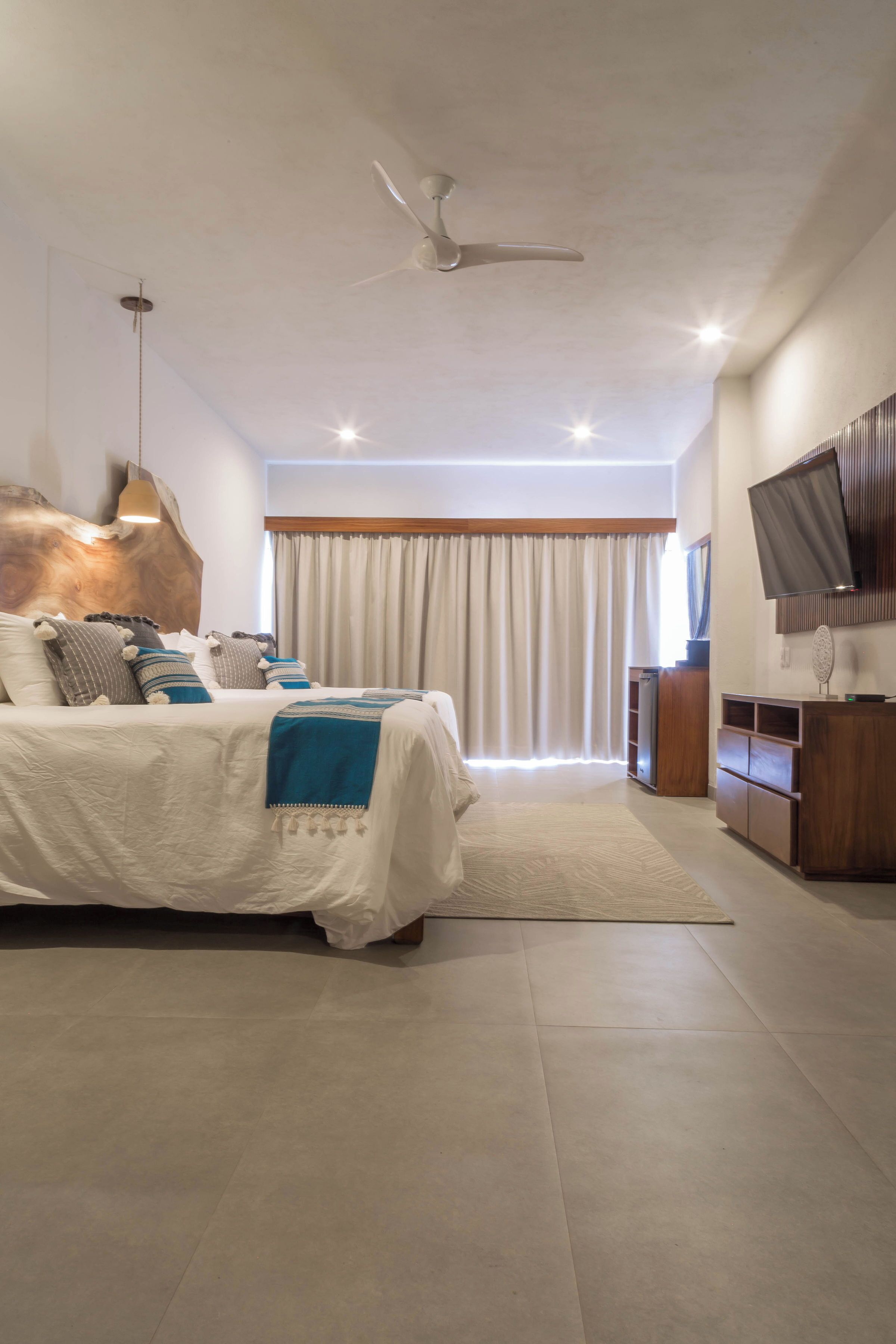 Ein modernes Schlafzimmer mit einem großen Bett, einem Deckenventilator, einem Fernseher und einem Holzkasten.