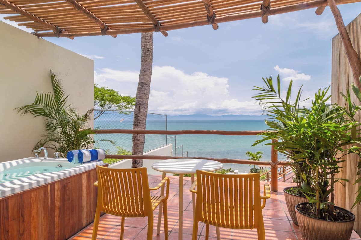 Un balcon agrémenté d’une pergola en bois, d’un jacuzzi, de deux chaises jaunes et de plantes en pot.