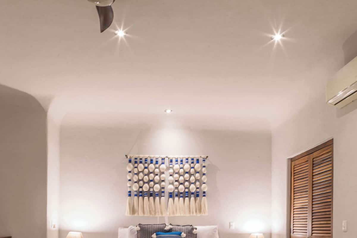 Une chambre à coucher avec un lit, des lampes de chevet, un ventilateur de plafond, une décoration murale à motifs et une armoire en bois.