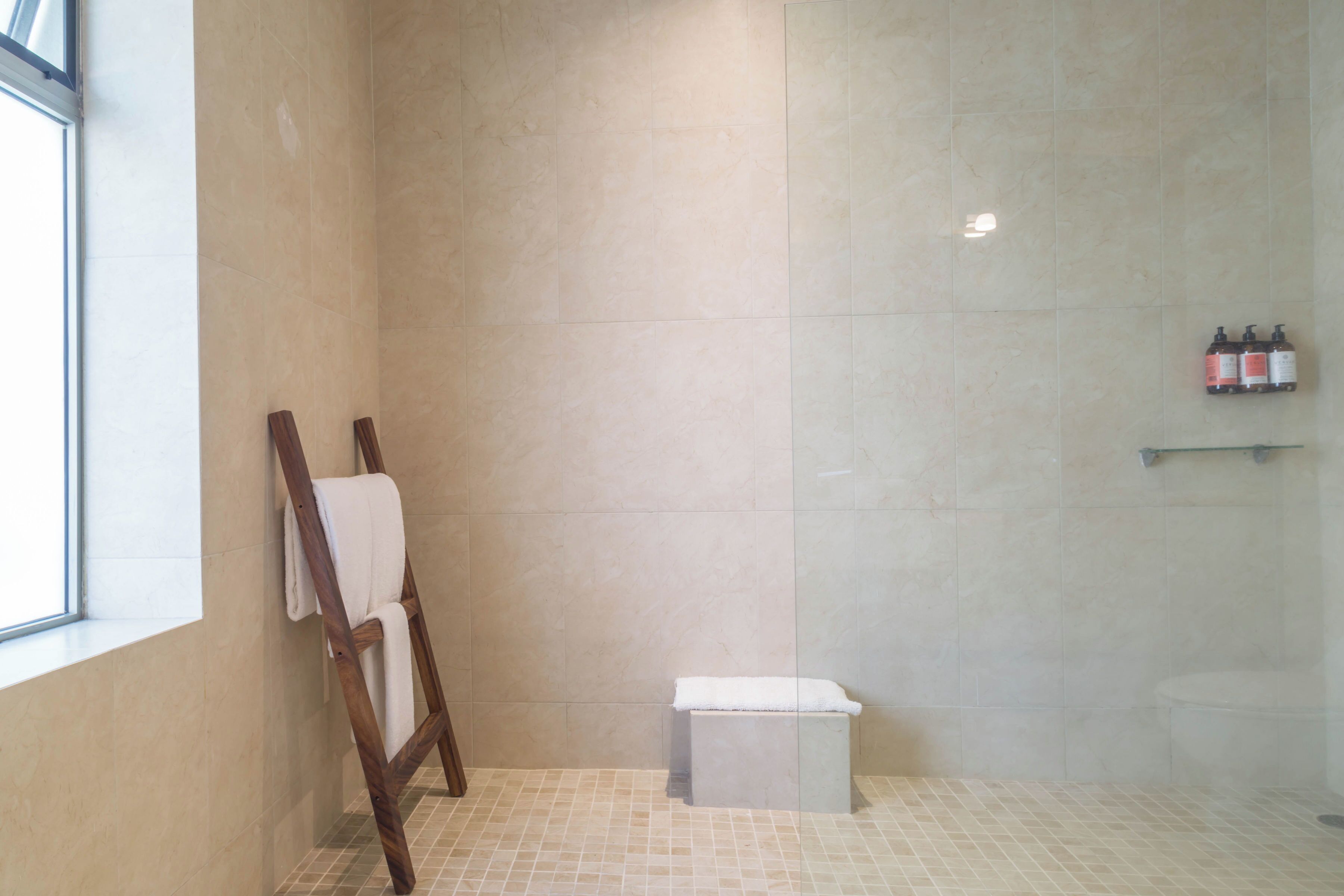 Une salle de bain avec une douche, une échelle en bois, un petit banc et une étagère contenant des articles de toilette.