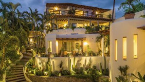 Un edificio de varios pisos con una escalera de piedra, rodeado de plantas tropicales y palmeras.