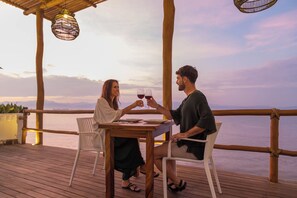 A couple sitting at a wooden table with a view of the sea, overlooking a wooden deck with a railing. - Hotel Ysuri Bucerias (Bucerías)