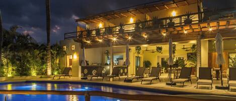 A poolside area with lounge chairs, a bar, and a covered seating area with potted plants.