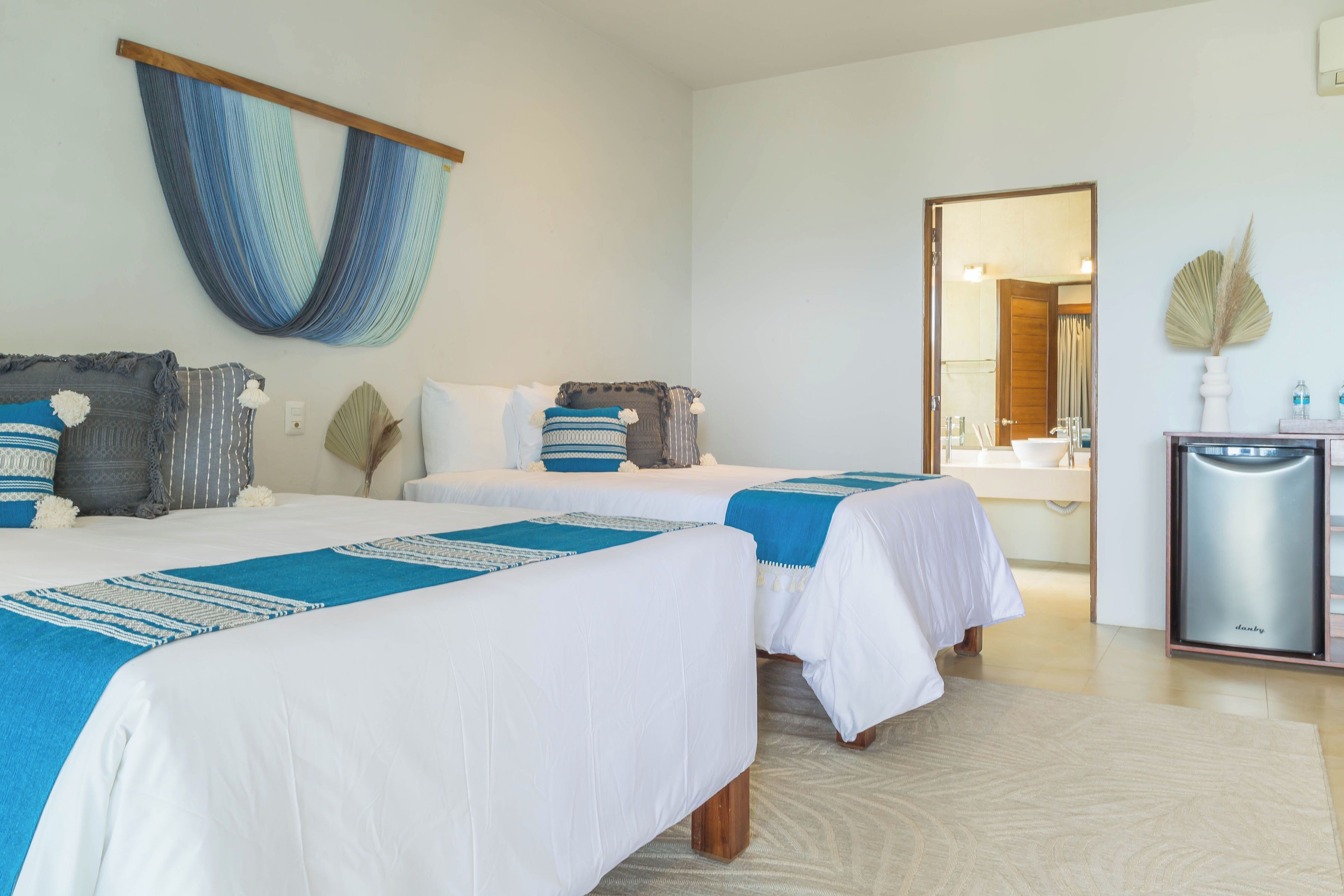A hotel room with two beds, a hammock, a minibar, and a large mirror.