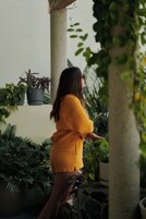 Una persona vestida de amarillo en un jardín con plantas en macetas y una pared de piedra.