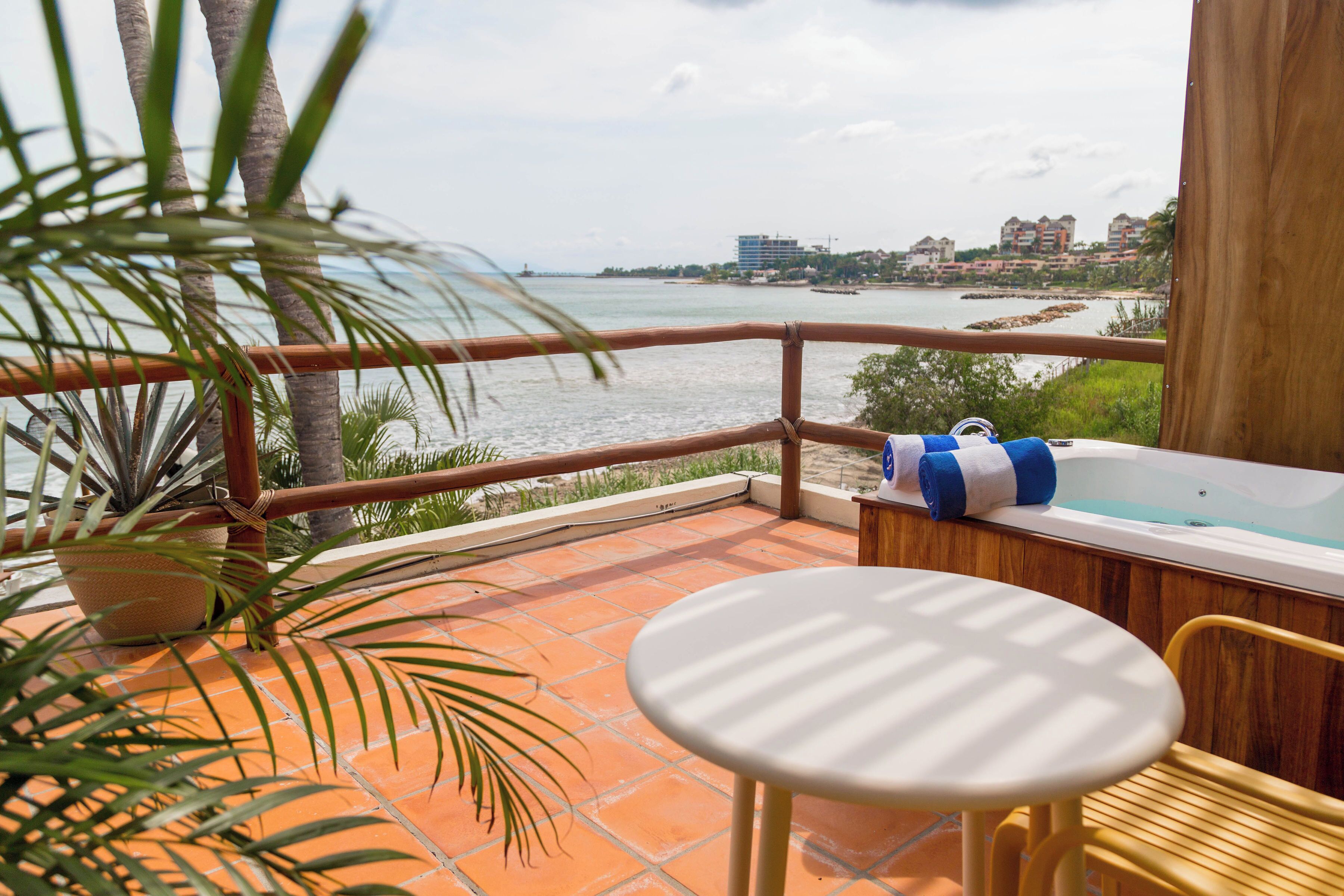 A balcony with a view of the sea, a wooden chair, a small table, and a hot tub.