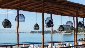 Un área junto a la piscina con una pérgola de madera, lámparas de mimbre colgantes y vista al mar.