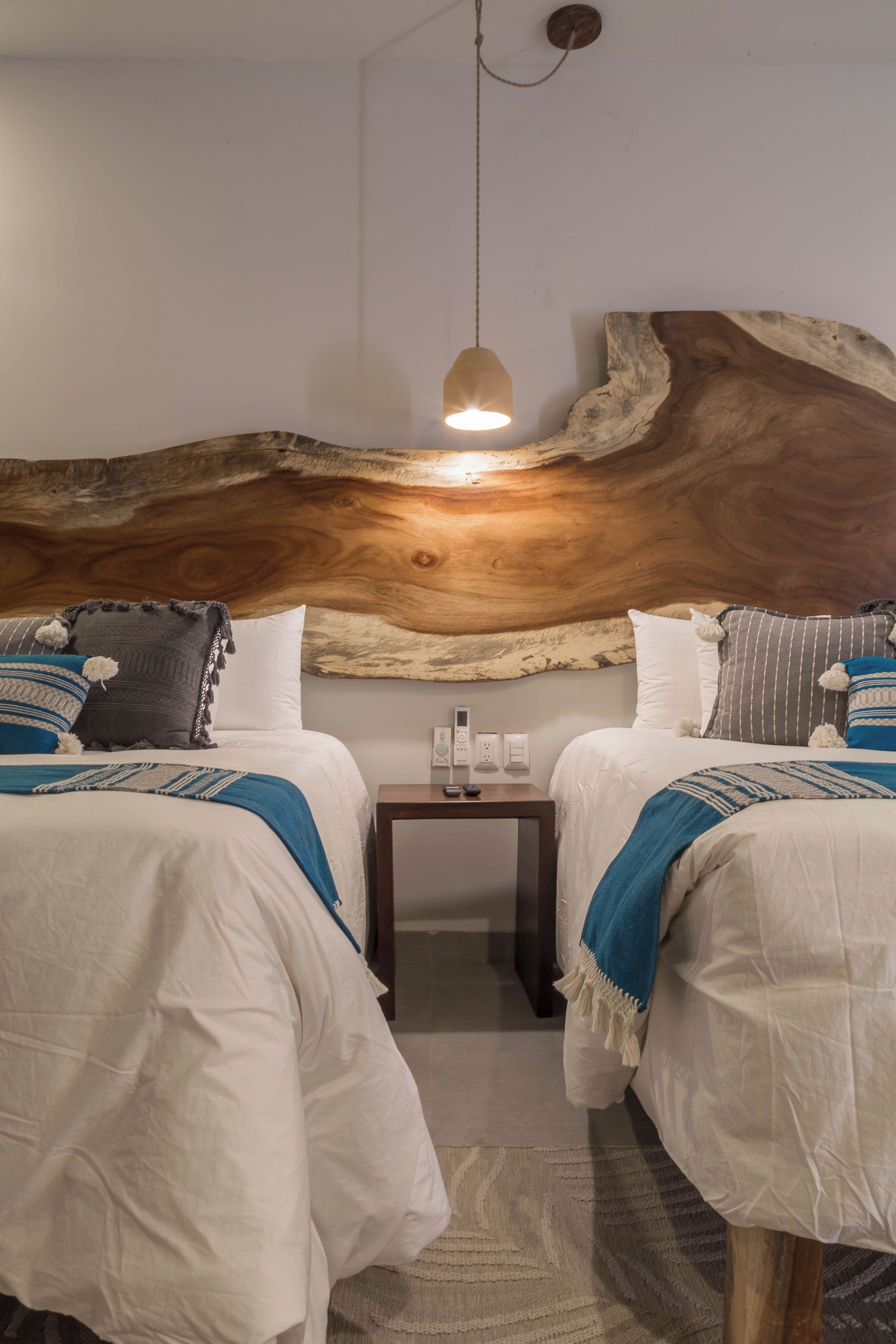 A room with two beds, a large wooden headboard, a small table with a lamp, and a wall-mounted light fixture.