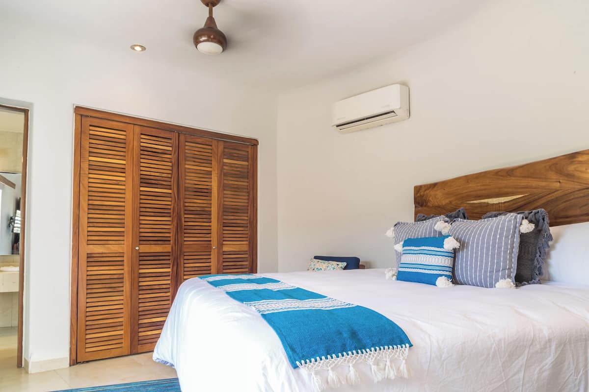 Une chambre avec un grand lit, une armoire en bois et un climatiseur fixé au mur.