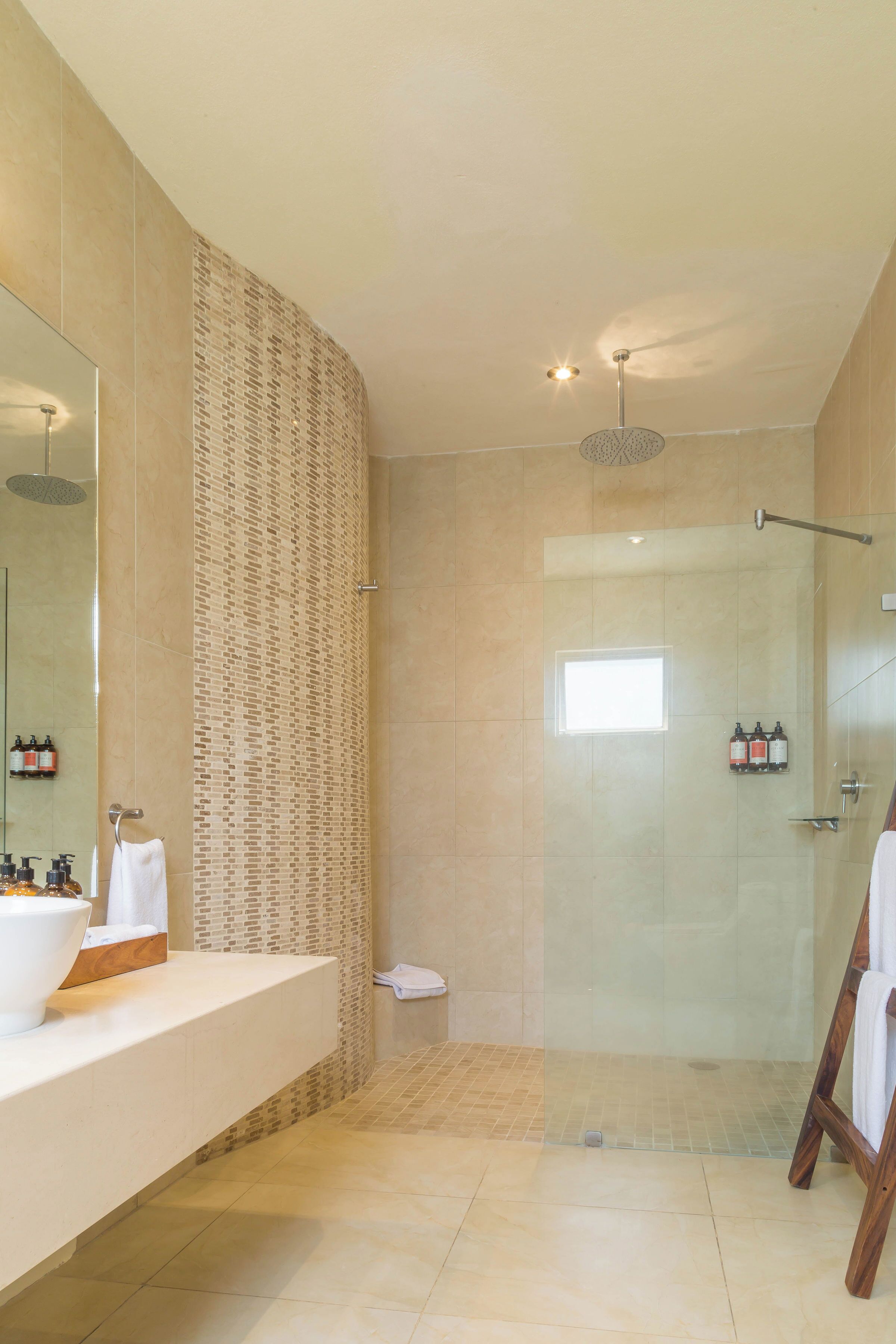 Een moderne badkamer met een grote spiegel, een douchegedeelte en een wastafel met toiletartikelen.