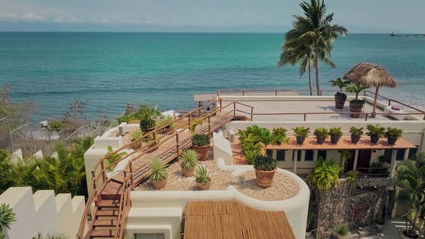 Una terraza en la azotea con cubierta de madera, plantas en macetas y vistas al océano.
