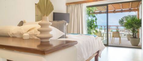 A hotel room with a bed, a desk, a TV, and a balcony with potted plants.