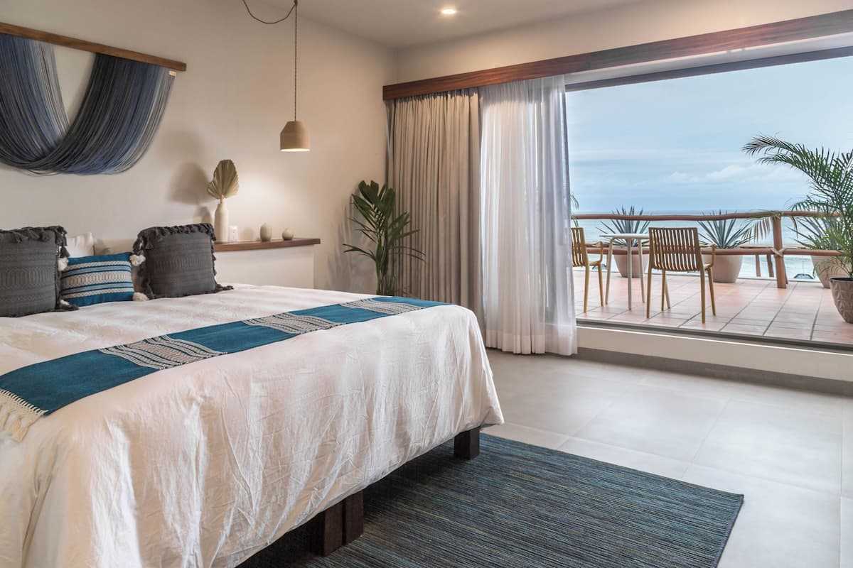 Une chambre avec un grand lit, un balcon avec des chaises et une vue sur la mer.