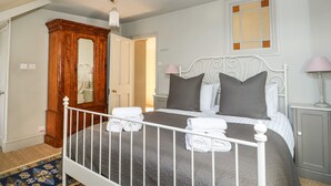 A bedroom with a bed, white headboard, bedside tables, a mirror, and a wardrobe. - Troon Cottage (Hunstanton)