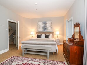 A bedroom with a bed, bedside lamps, a bench, a dresser, and a mirror. - Troon Cottage (Hunstanton)