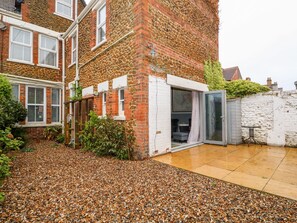 A residential building with a stone facade, a small patio area with pebbles, and a sliding glass door leading to an outdoor seating area. - Troon Cottage (Hunstanton)
