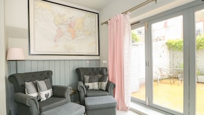 A room with two grey armchairs, a large world map on the wall, and a sliding glass door leading to an outdoor area. - Troon Cottage (Hunstanton)