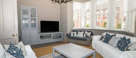 A living room with a television, grey cabinets, a chandelier, and two sofas with patterned cushions.