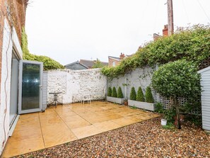A patio with a tiled floor, a small table, a chair, and a white door. - Troon Cottage (Hunstanton)