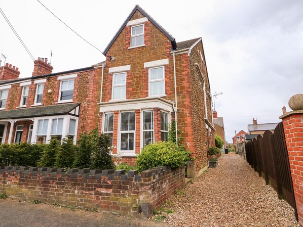 A two-story brick house with a white front door, a bay window, and a small front garden. - Troon Cottage (Hunstanton)