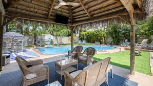 Un'area esterna coperta con piscina, mobili in vimini e una ventola a soffitto.