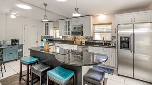 Una cucina moderna con isola centrale, sgabelli da bar, elettrodomestici in acciaio inossidabile e illuminazione a sospensione.