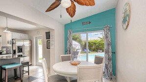 Una cucina con frigorifero, zona pranzo con tavolo e sedie, e vista su una piscina attraverso una finestra.