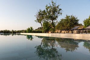 A serene swimming pool with clear water reflecting trees and a clear sky. - Citrus Grove (Rethymno)