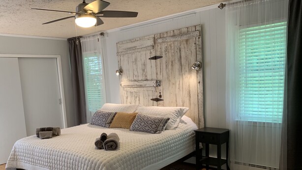 Une chambre avec un grand lit, un ventilateur de plafond, une tête de lit rustique et des tapis à motifs.
