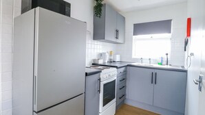 A compact kitchen with a refrigerator, stove, microwave, and a window with a view. - California Summers (Great Yarmouth)