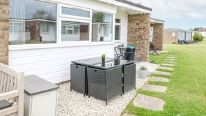 A modern house with a patio area featuring a glass table and wicker chairs. - California Summers (Great Yarmouth)