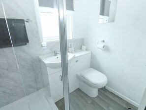 Un baño moderno con cabina de ducha de vidrio, un lavamanos blanco, inodoro y pared con azulejos de mármol.