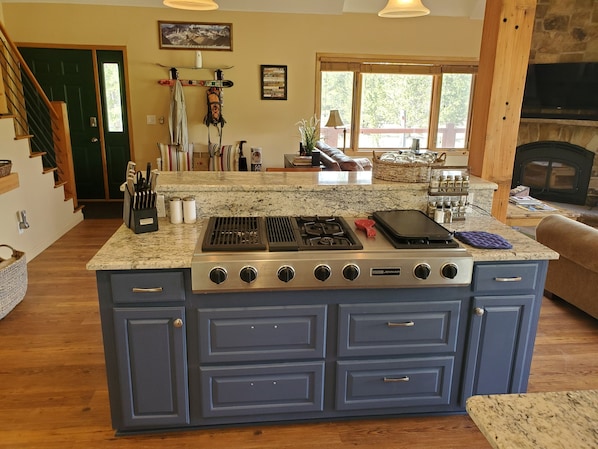 A kitchen with a central island stove, wooden cabinets, and a view of the outdoors through large windows.