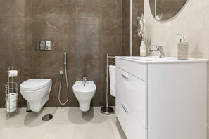 Een moderne badkamer met toilet, bidet en een wastafelmeubel met spiegel en wastafel.