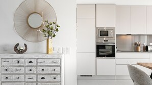 A modern kitchen with white cabinetry, a microwave, and an oven. There is a decorative mirror on the wall and a vase with a plant on a dresser. - Casa Urlaub - Panoramic Rooftop View (Nazaré)