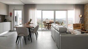 A modern living room with a dining area, large windows, and a view of the city. - Casa Urlaub - Panoramic Rooftop View (Nazaré)