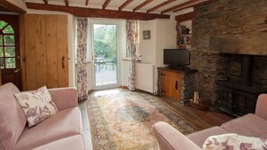 Una sala de estar acogedora con chimenea de piedra, vigas de madera, un televisor y un tapete estampado.
