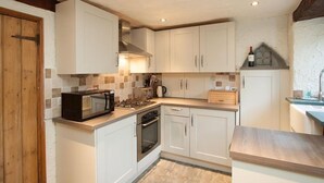 Una cocina compacta con gabinetes blancos, microondas, estufa y pileta.