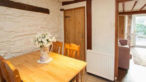 Un comedor con una mesa y sillas de madera, un jarrón con flores, una pared de piedra y una puerta de madera.