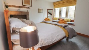 A neatly made bed with a lamp, a window with curtains, and a wooden headboard. - 2 The Square (Skipton)
